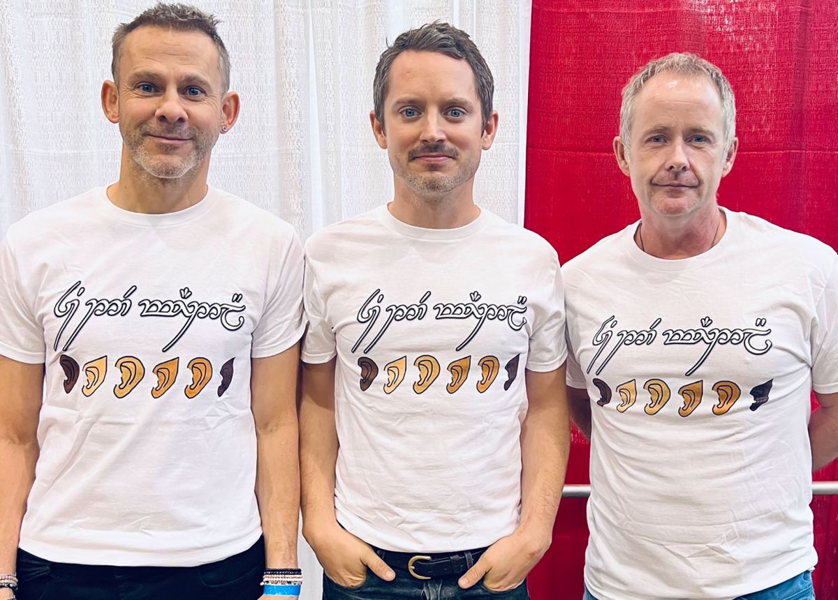 Elijah Wood (Frodo) Dominic Monaghan, (Merry) y William Nathan Boyd (Pippin) usando una playera blanca con ilustración de orejas élficas de distintas razas